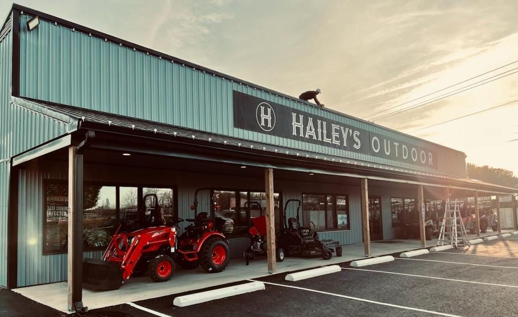 Hailey's Outdoors storefront with tractors on display under the awning. A person is on the roof.