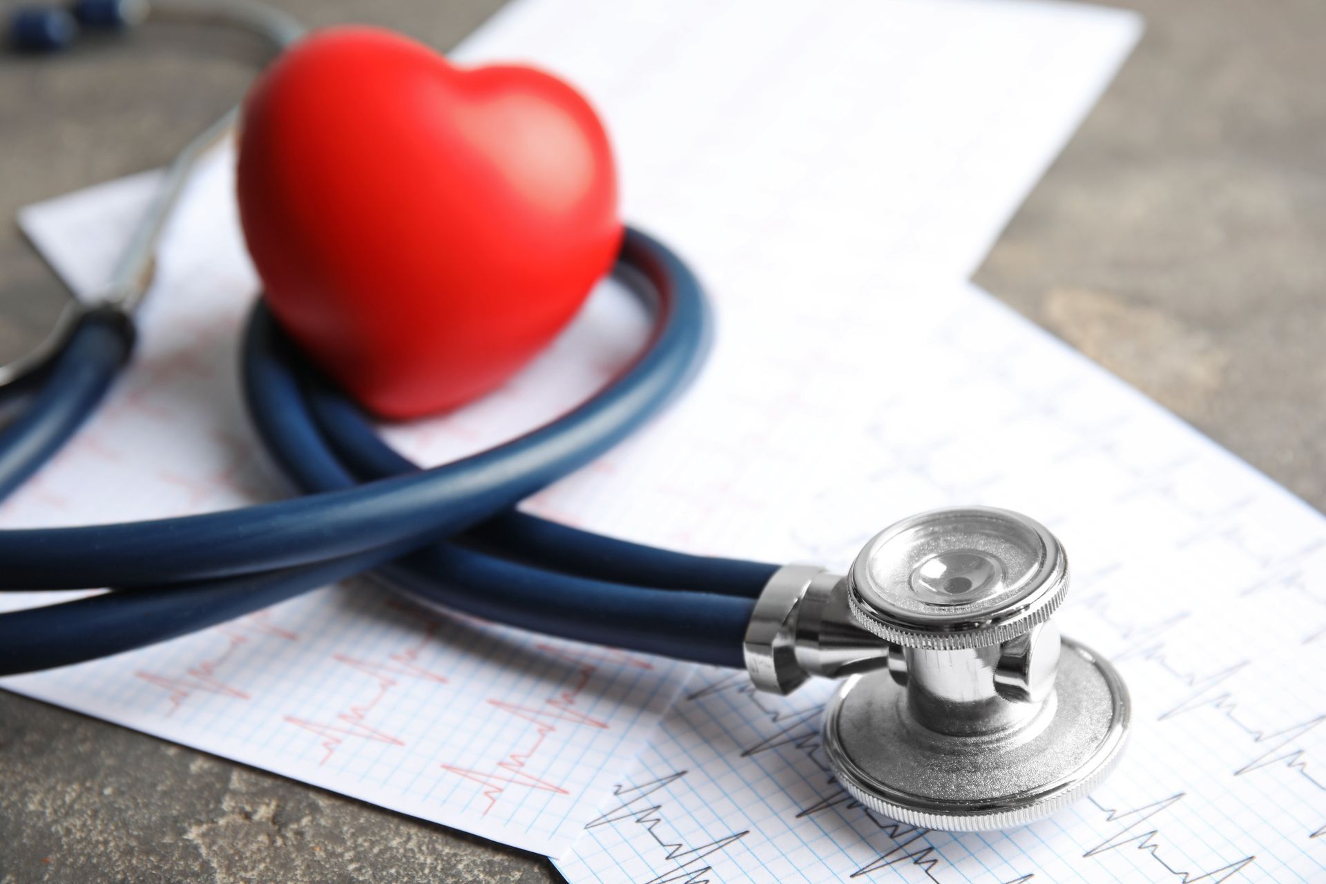 A red heart is sitting on top of a stethoscope on a piece of paper.
