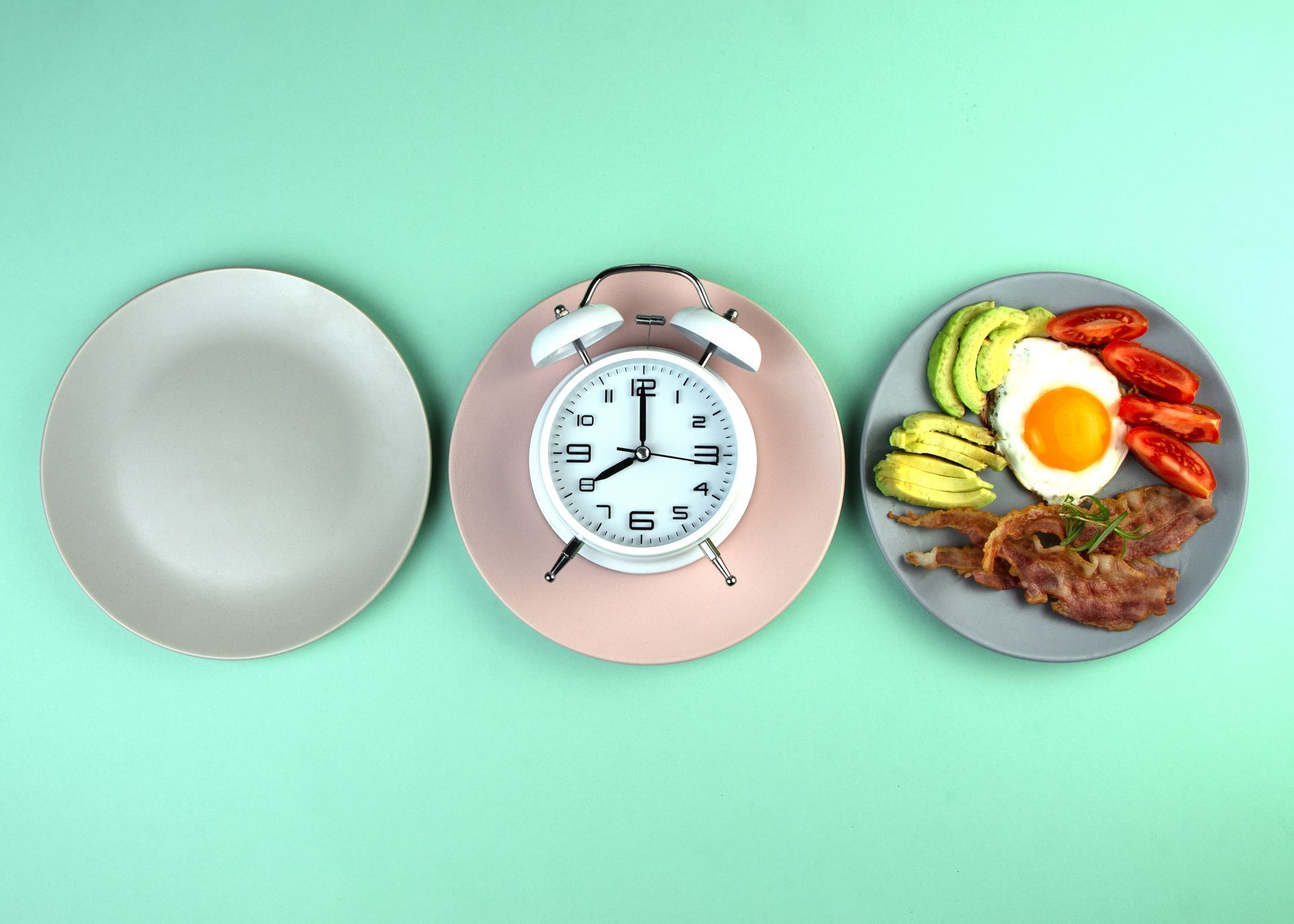 Three plates of food and an alarm clock on a green background.