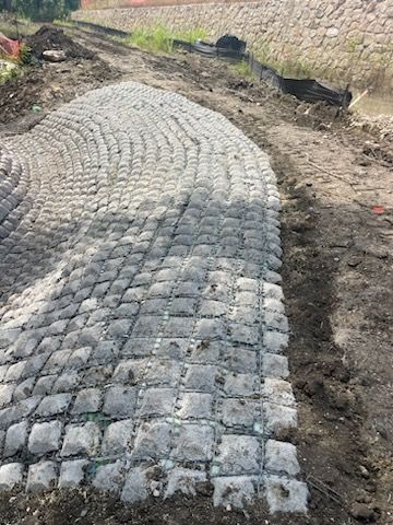 Curved cobblestone path under construction beside a stone retaining wall.