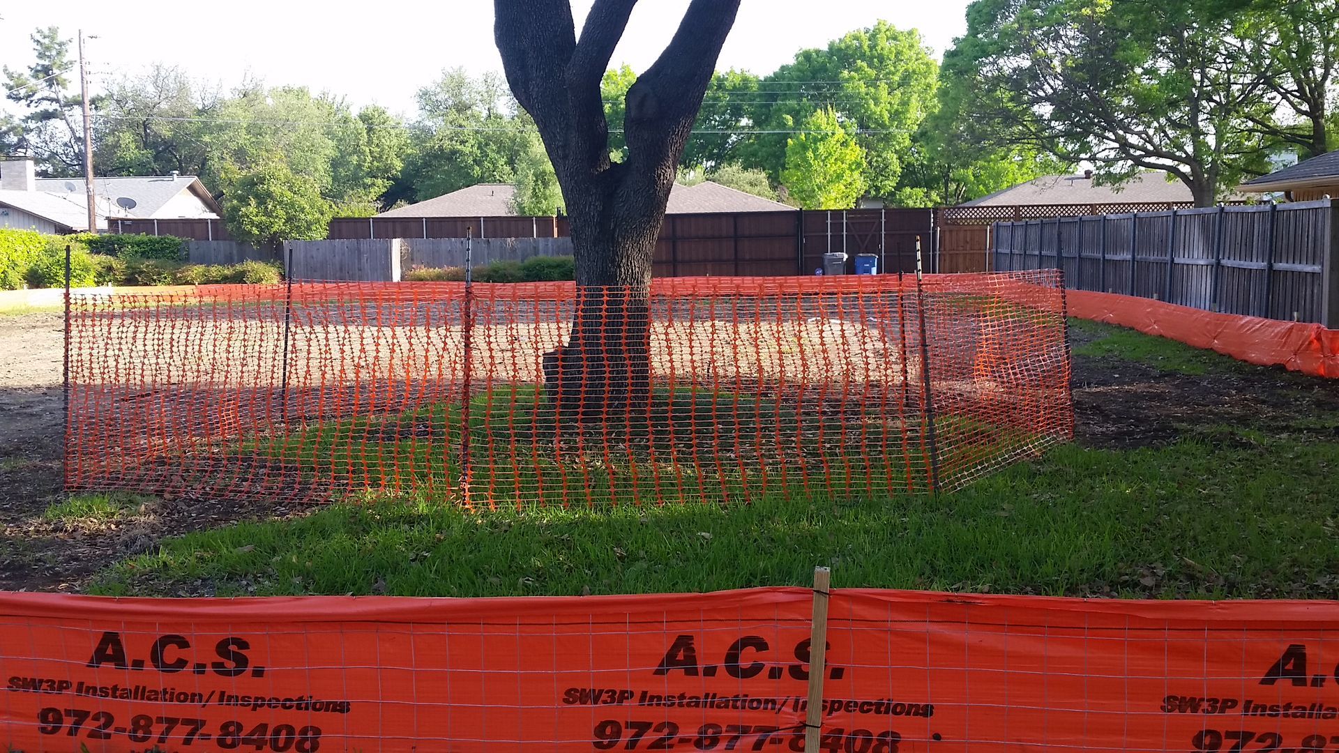 Backyard fenced off with orange construction mesh around a tree and grassy area.