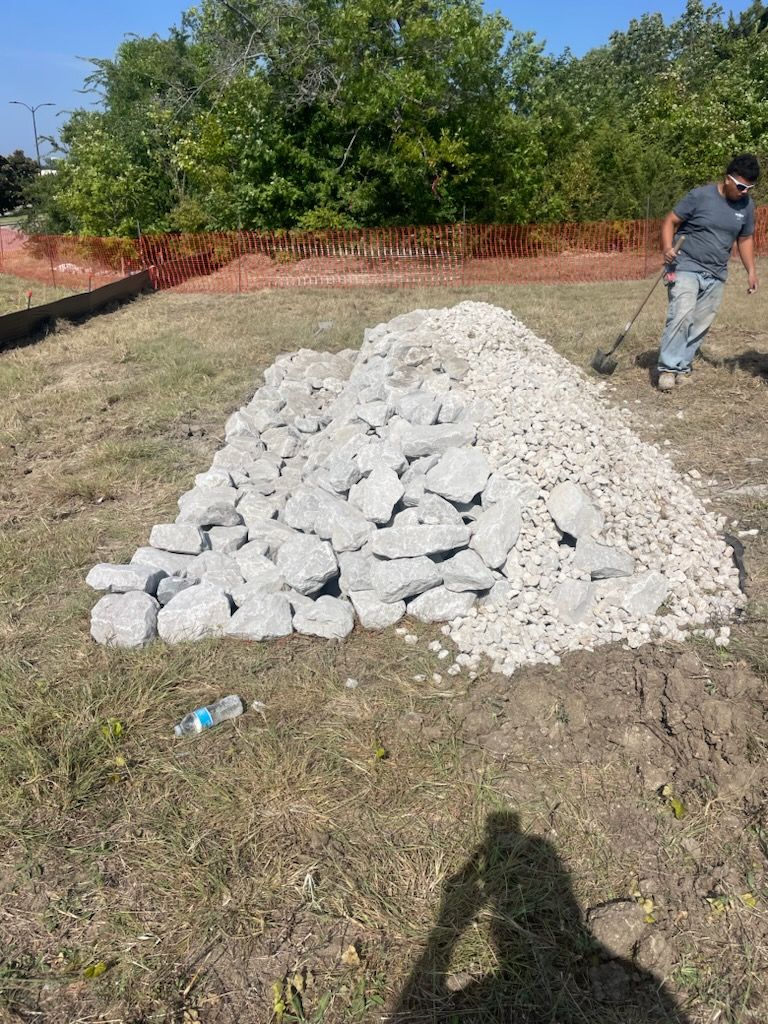 Pile of white rocks in a grassy yard, with a person standing nearby and a brick wall in the background.