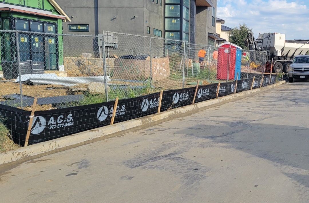 Construction area with black safety barriers, a red portable toilet, and a building under construction