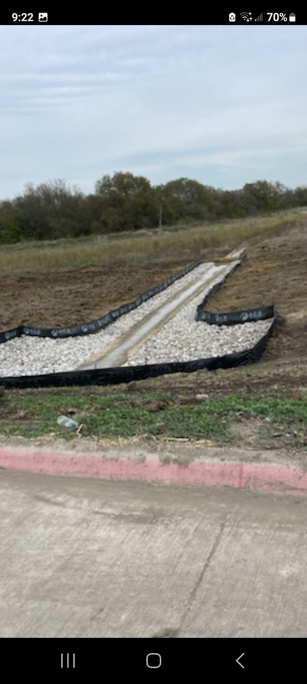 Broken white concrete slab on a grassy roadside with a pink curb and cloudy sky overhead