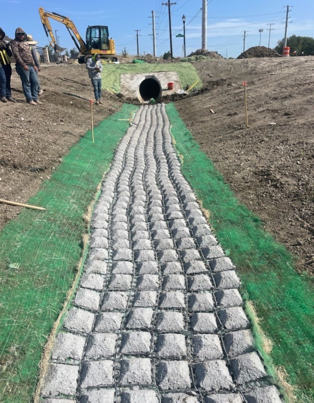 Construction site with a stone-lined drainage path leading to a culvert pipe under an embankment
