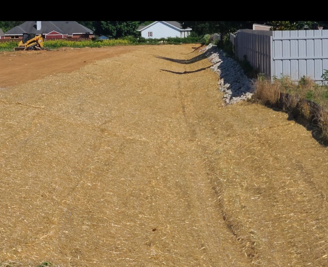 Wide dirt lot under development beside a white fence, with houses in the distance.
