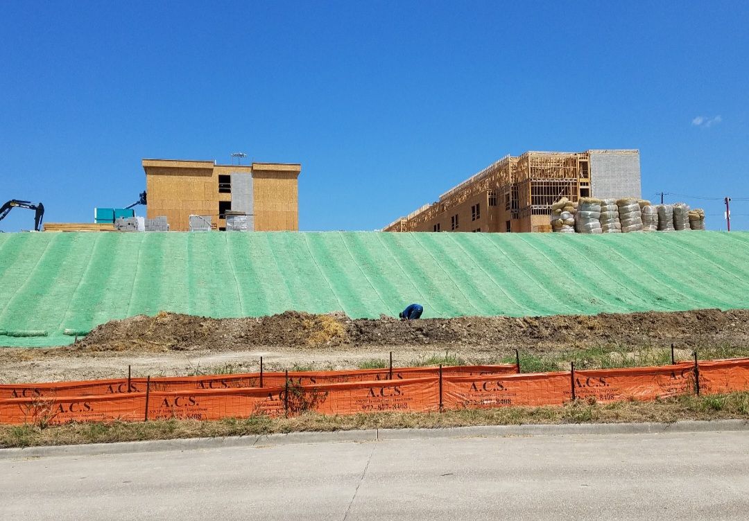 Construction site on a grassy slope with building materials and wooden structures under a clear blue sky