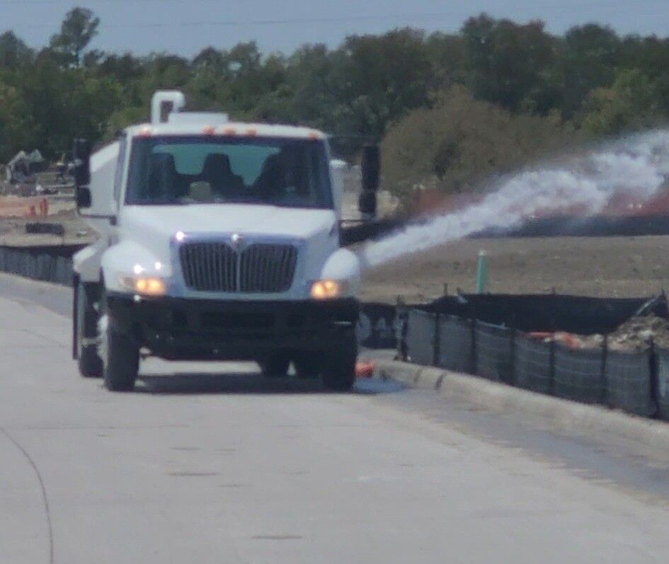 White utility truck spraying water on a roadway beside a construction barrier