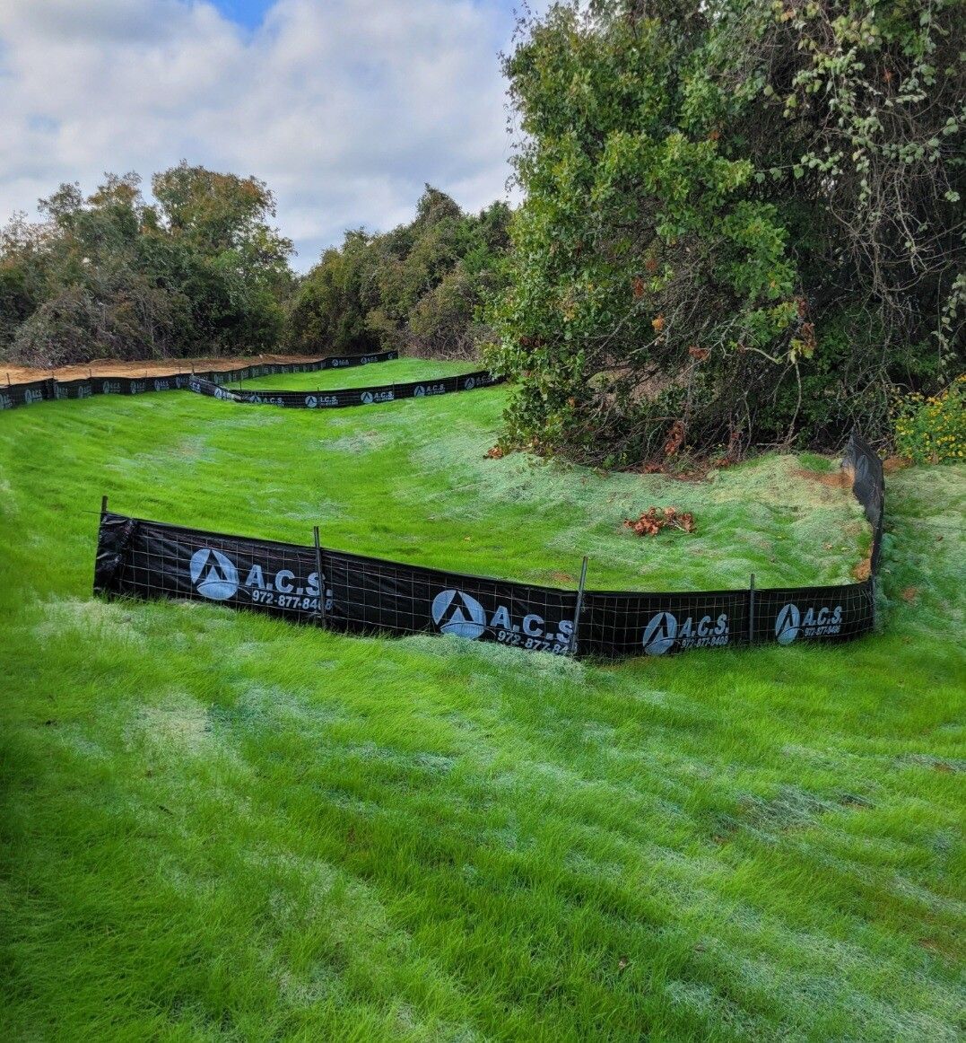 Grassy park landscape with a black barrier fence and trees under a cloudy sky