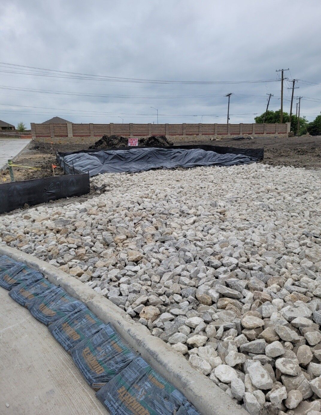 Construction site with a gravel embankment and black geotextile lining under an overcast sky