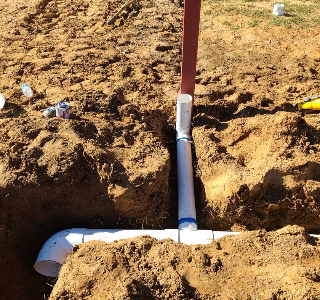 White PVC pipe installation in a dirt trench with a vertical red post above it.