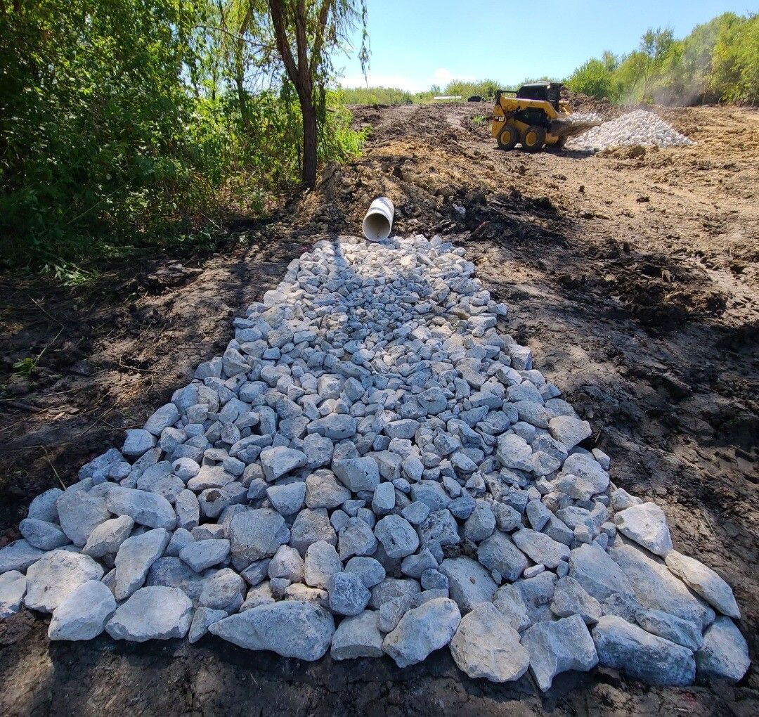 Gravel piled on a dirt path at a construction site, with a bulldozer in the background
