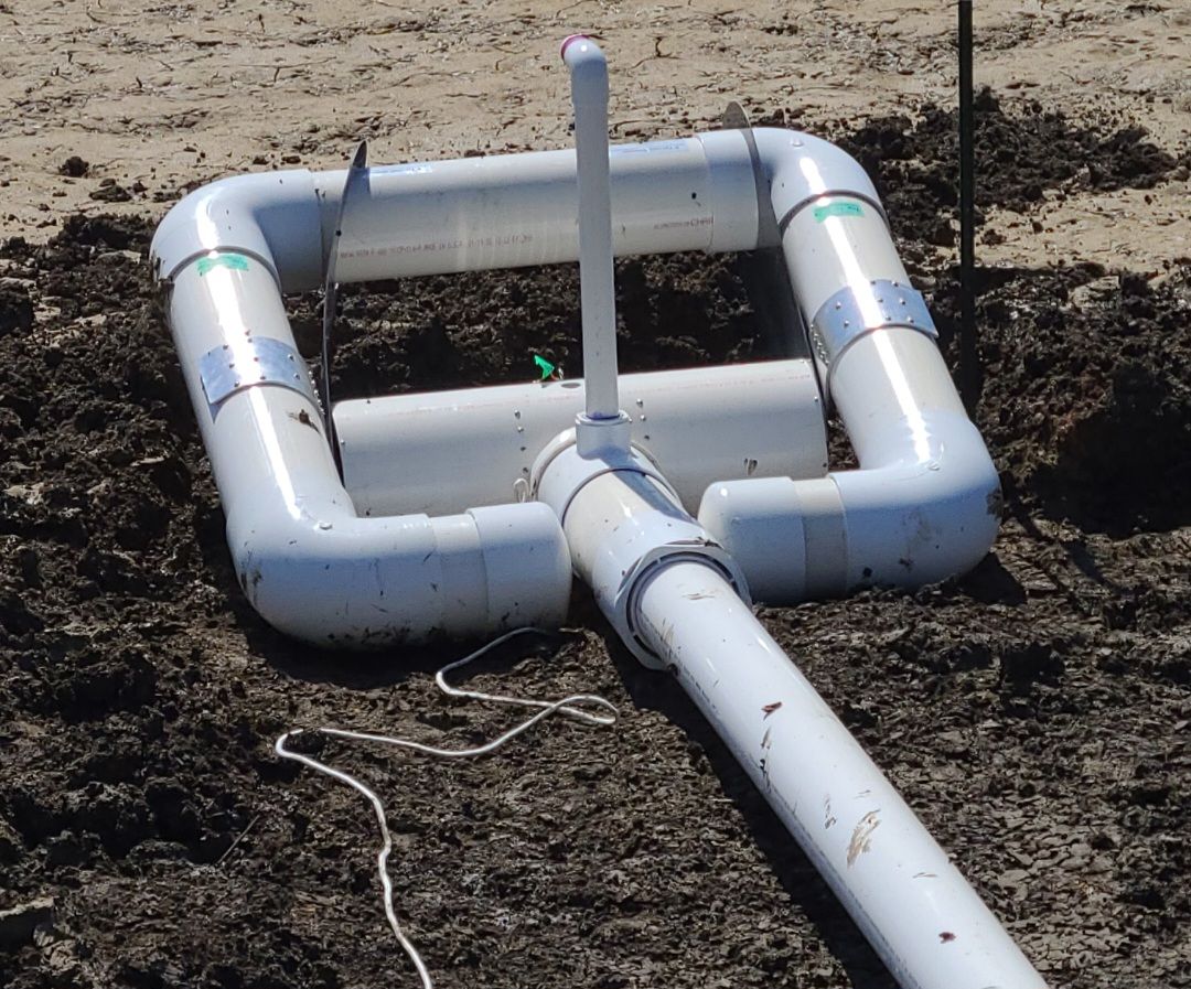 White PVC pipe frame and drainage pipe laid on dirt outdoors