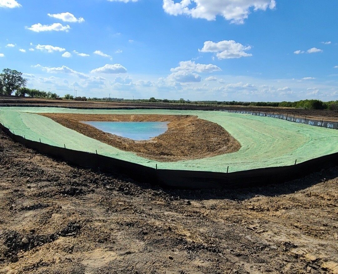 Vegetated pond basin in a field under a blue sky, with a small water pool in the center