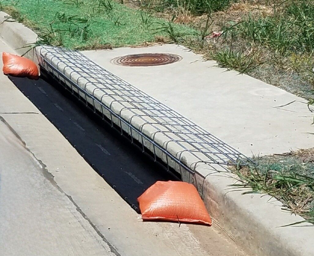 Orange sandbags blocking a storm drain beside a sidewalk and grassy curb