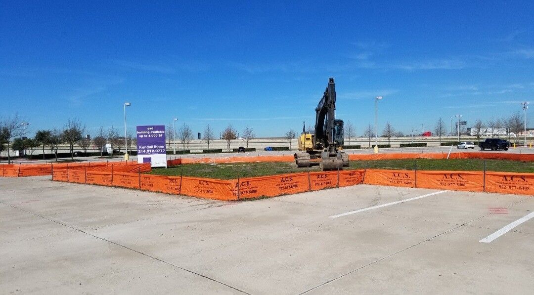 Construction site with orange safety fencing, a drilling rig, and a purple sign under a clear blue sky