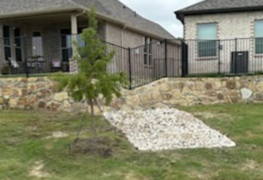 Two houses with stone retaining wall, black fence, and small tree in front yard