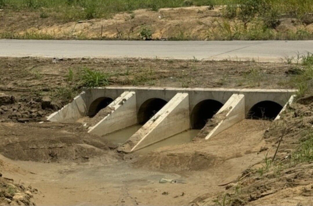 Concrete drainage culvert under a road, with muddy runoff and dry banks around it