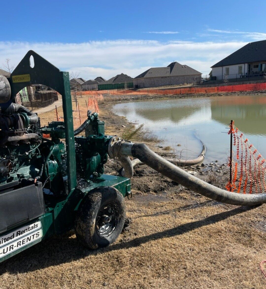 Small green pump by muddy pond at a construction site with houses in the background