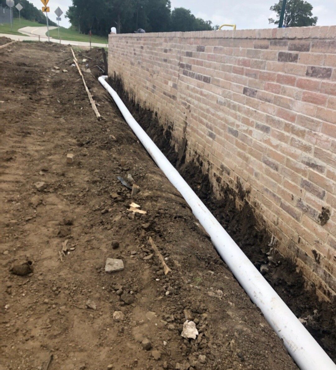 White pipe laid along dirt trench beside a brick retaining wall.