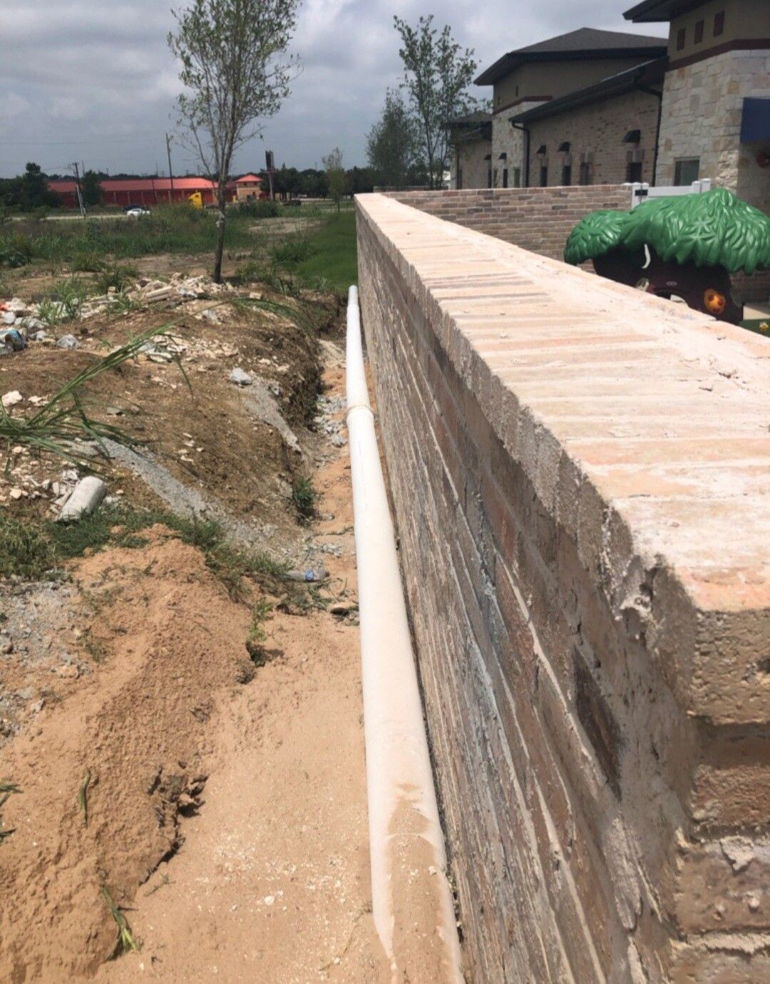 Long brick wall beside a sandy path and construction site near a house