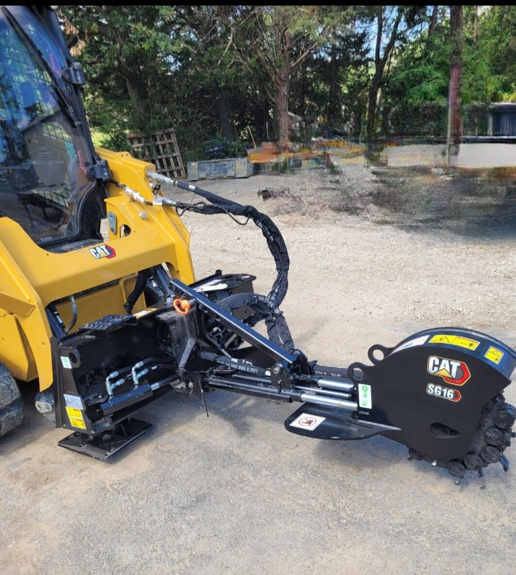 Yellow construction machine with a black CAT stump grinder attachment on gravel outdoors