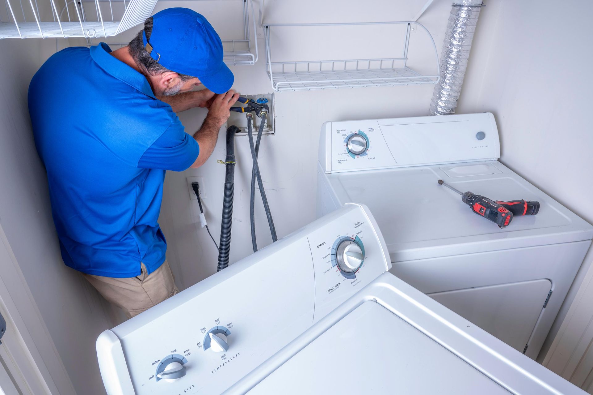 Plumber installing water supply lines behind a washing machine in a laundry room. Plumber installing water supply lines behind a washing machine in a laundry room.