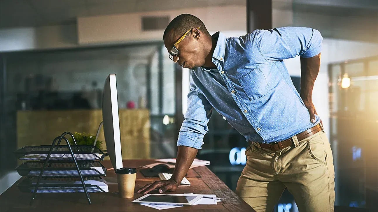 Man in a blue shirt leaning over papers at a desk in a modern office
