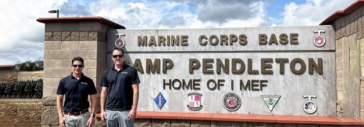 Two people standing beside the Marine Corps Base Camp Pendleton entrance sign.