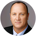 Headshot of a person in a dark suit and light blue shirt on a gray background