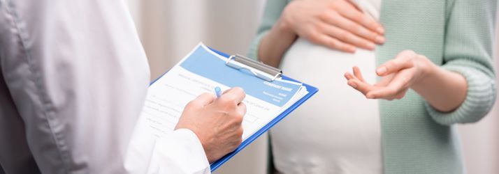 Doctor writing on a clipboard while speaking with a patient in a bright clinic