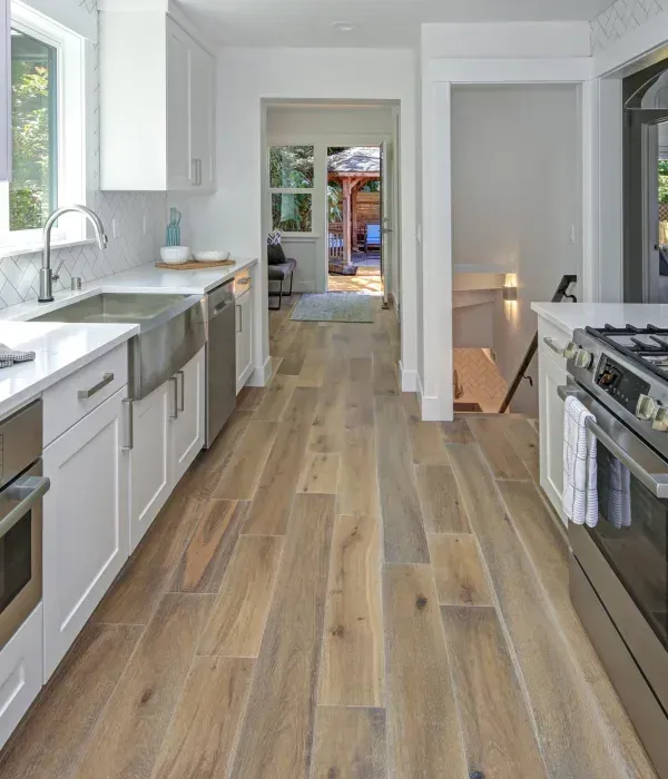 Bright modern kitchen with white cabinets, wood floors, and a view into the backyard through a doorway.