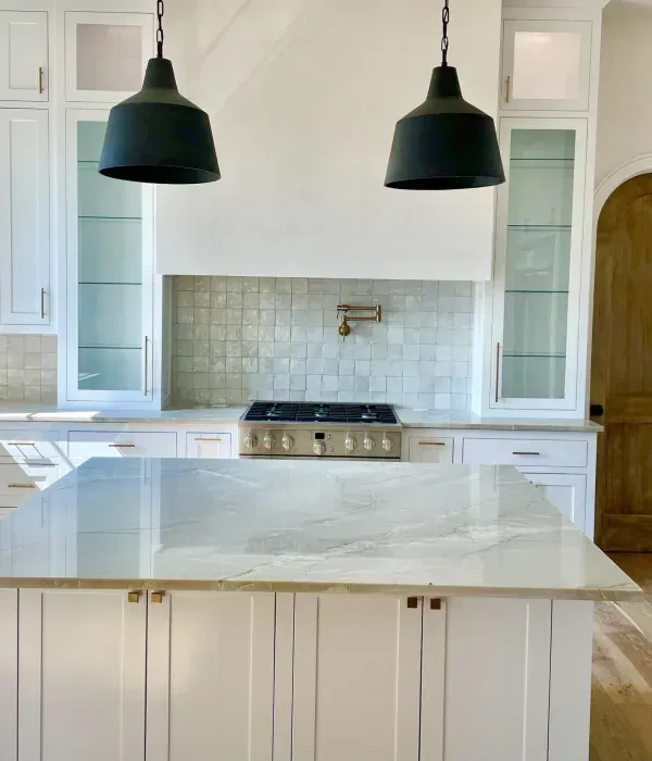 Bright white kitchen with marble island, black pendant lights, and stainless steel stove.