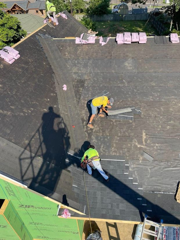 Two workers in yellow vests on a roof near pink insulation boards and a large crane shadow