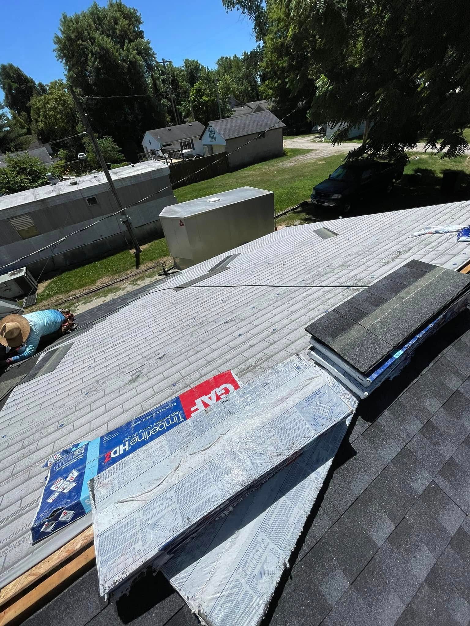 Roof shingles and trim pieces laid out on a sloped rooftop with trees and houses in the background