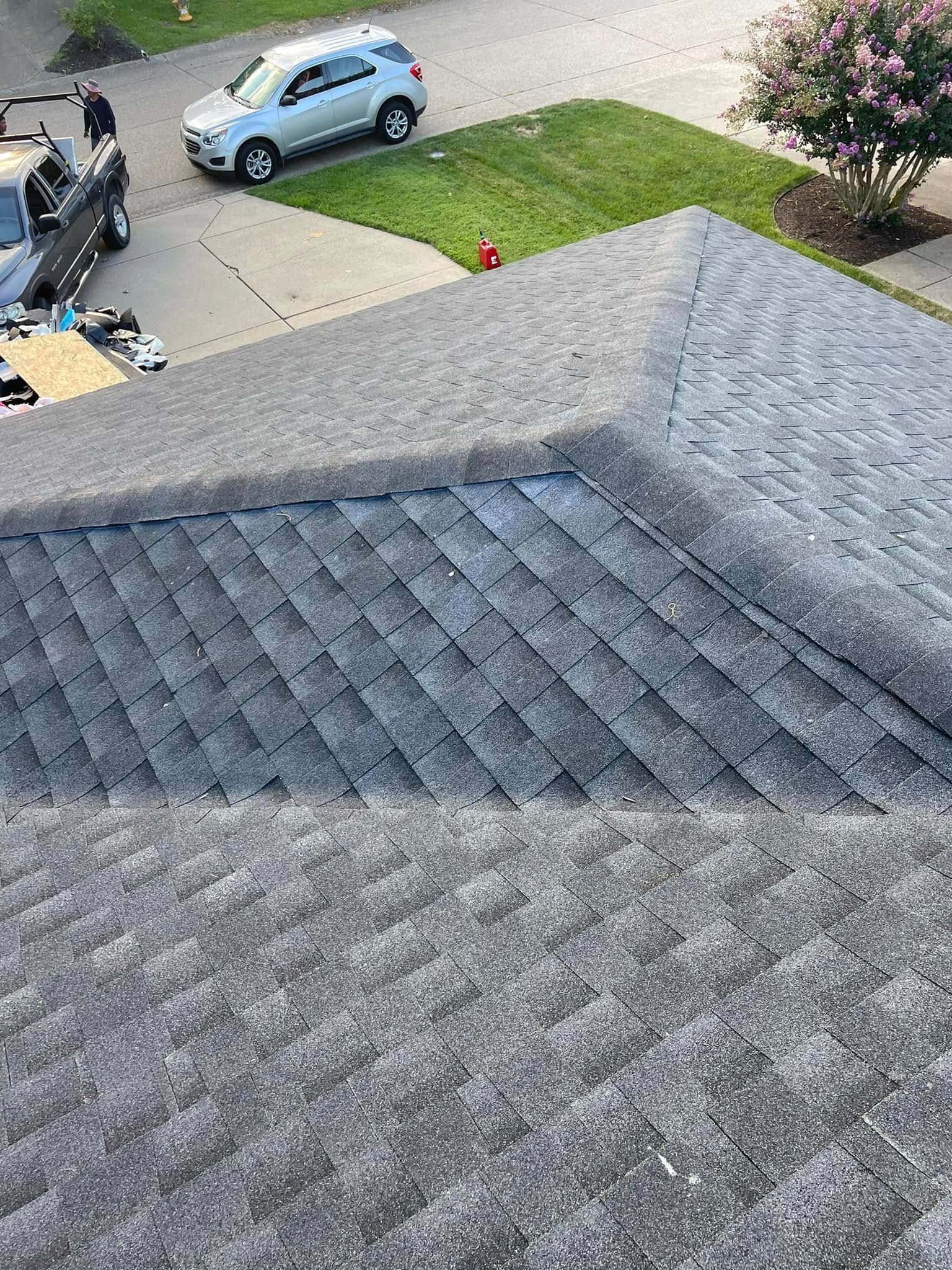 Roof shingles overlooking a driveway with a blue car, lawn, and sidewalk below