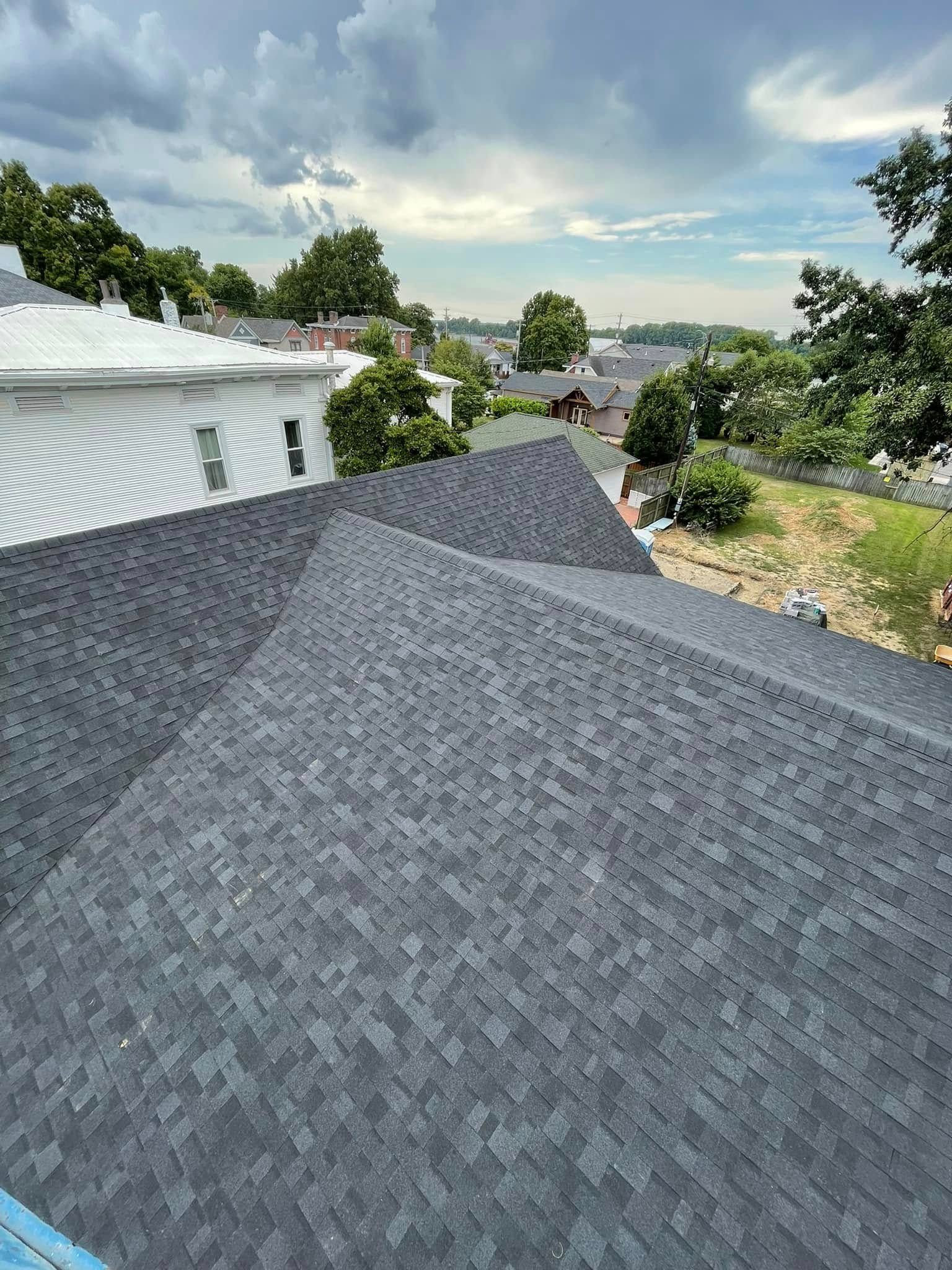 Gray shingled roof overlooking trees and distant water under a cloudy sky
