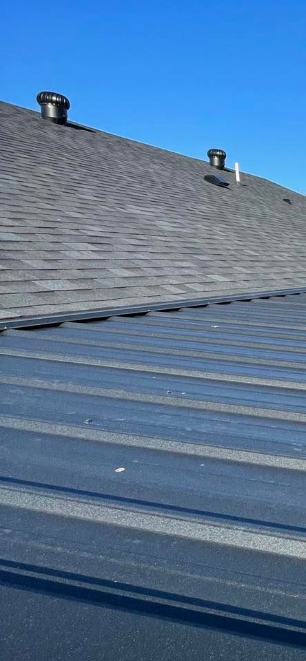 Blue metal roof in foreground with gray shingled roof and two vents under a clear sky