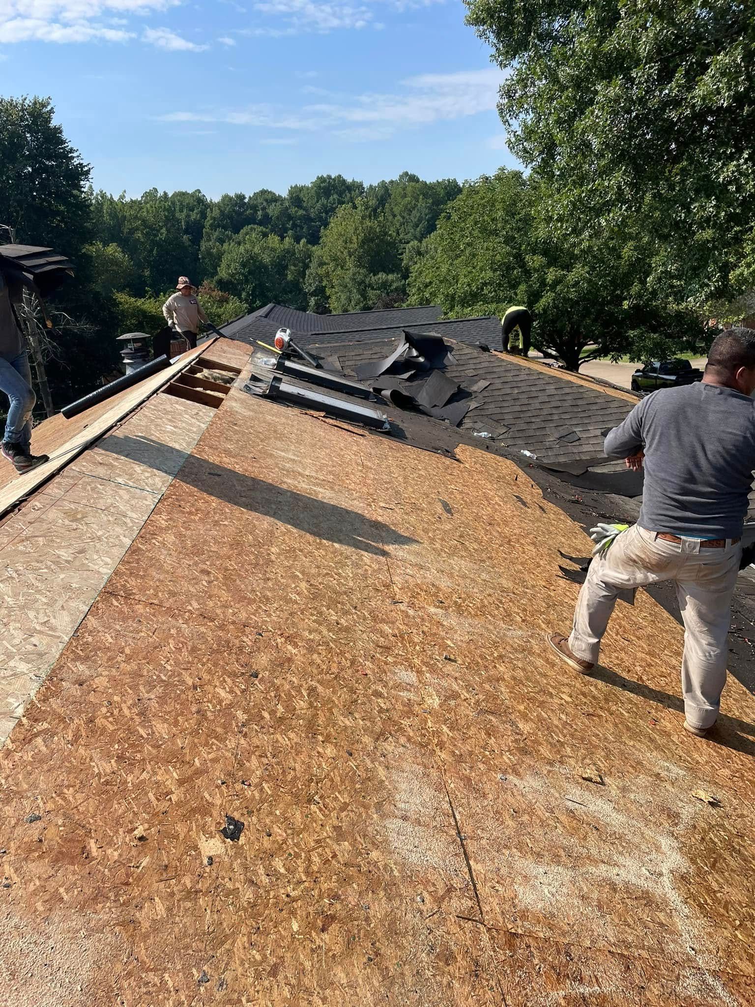 Workers repair a roof, exposing plywood and underlayment beside torn shingles.
