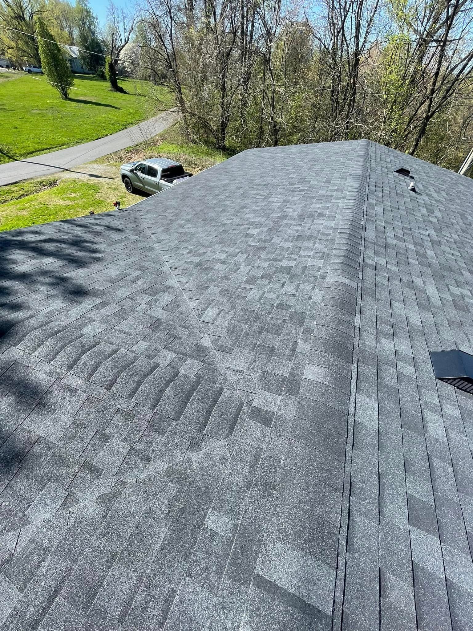 Gray shingled roof with trees and a grassy yard in the background