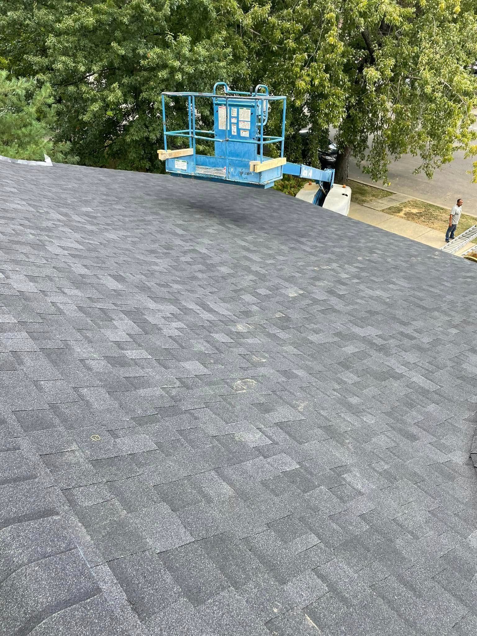 Blue lift platform beside a tree over a gray roof edge