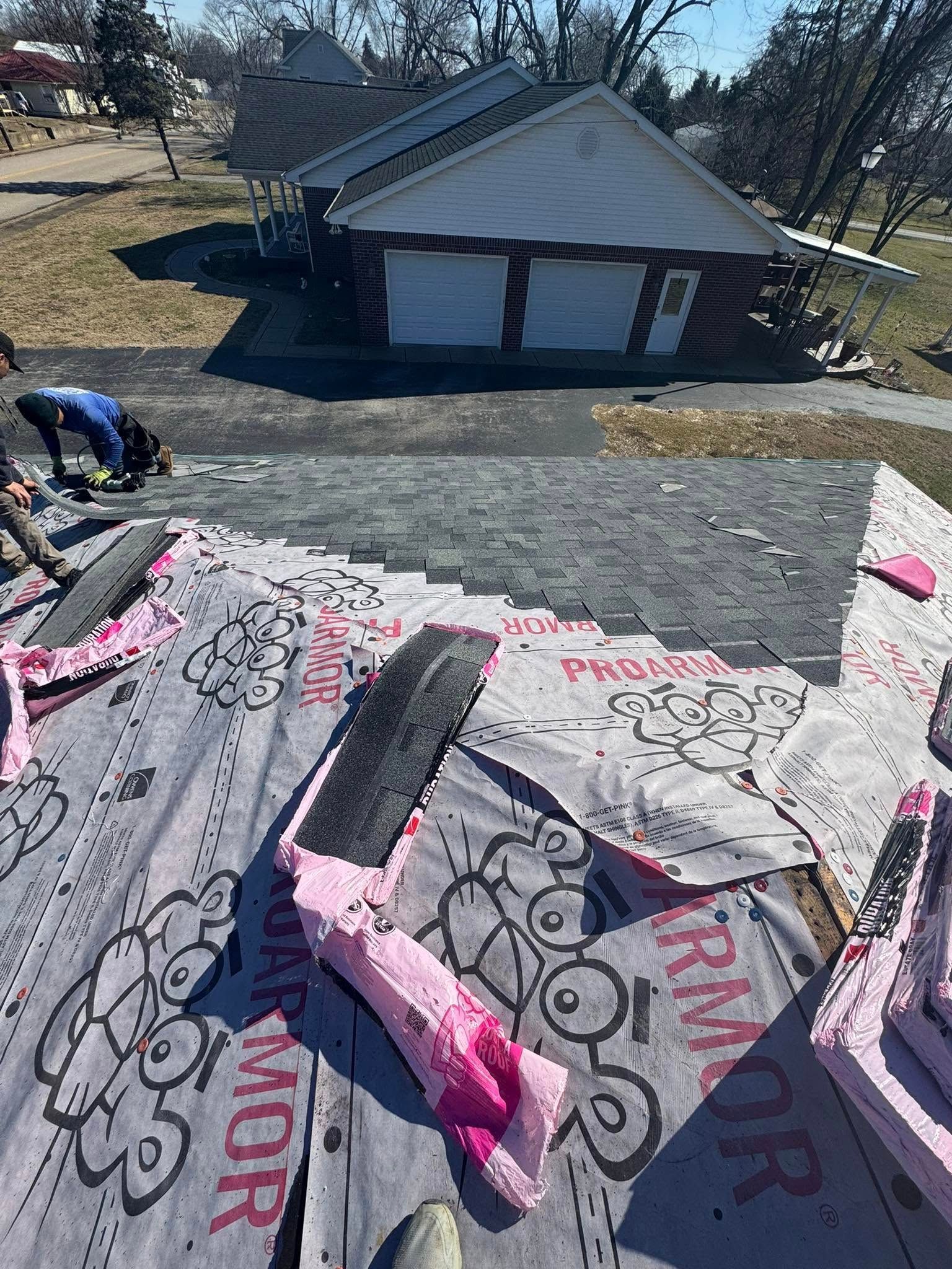 Roofing materials laid on a roof with a house and yard in the background.