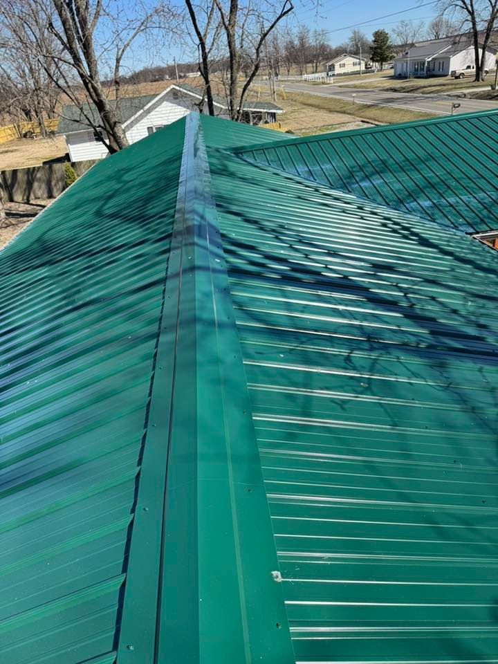 Green metal roof with a ridge line, seen from above on a sunny day