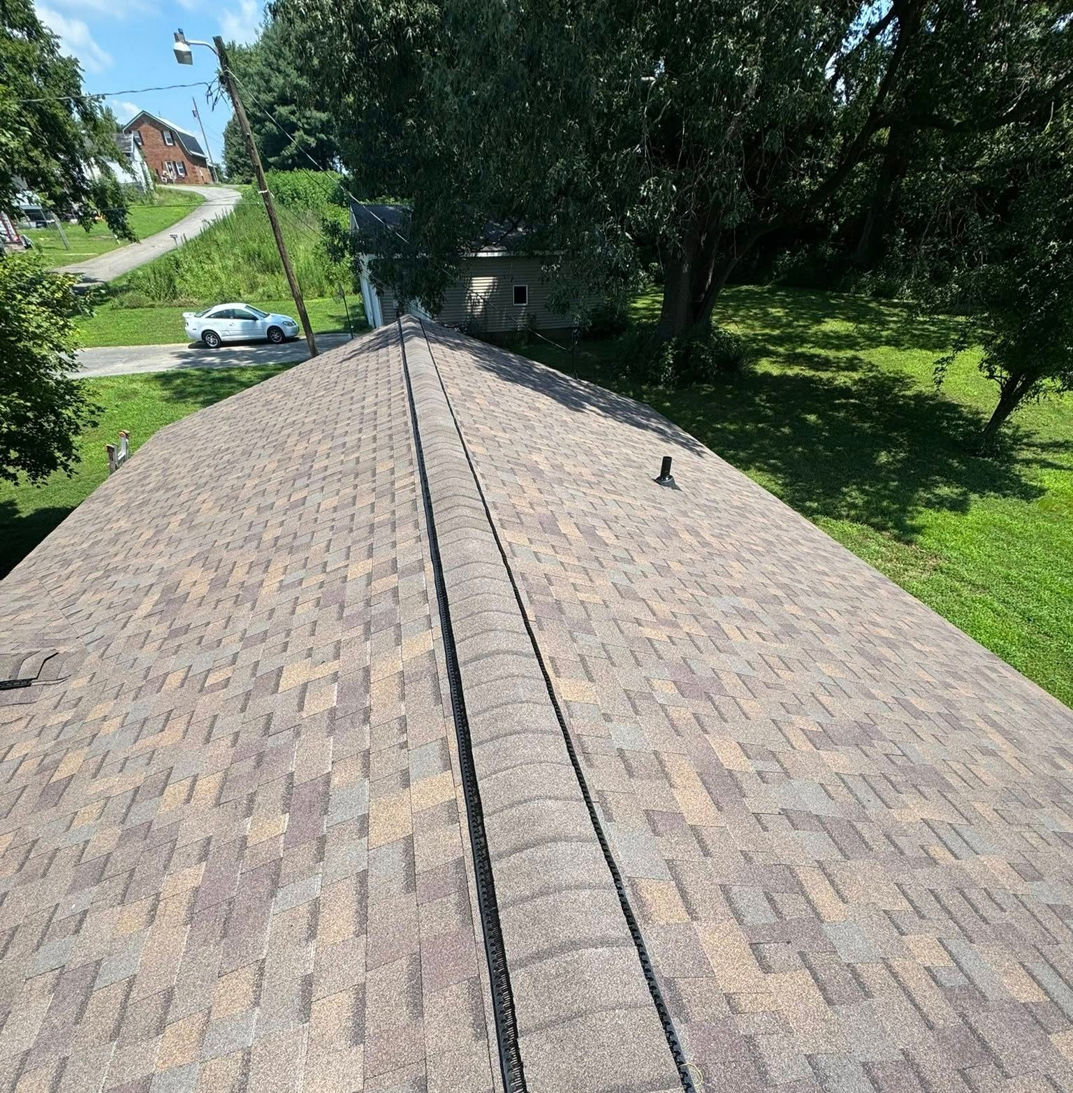 Aerial view of a shingled roof with trees and a street in the background