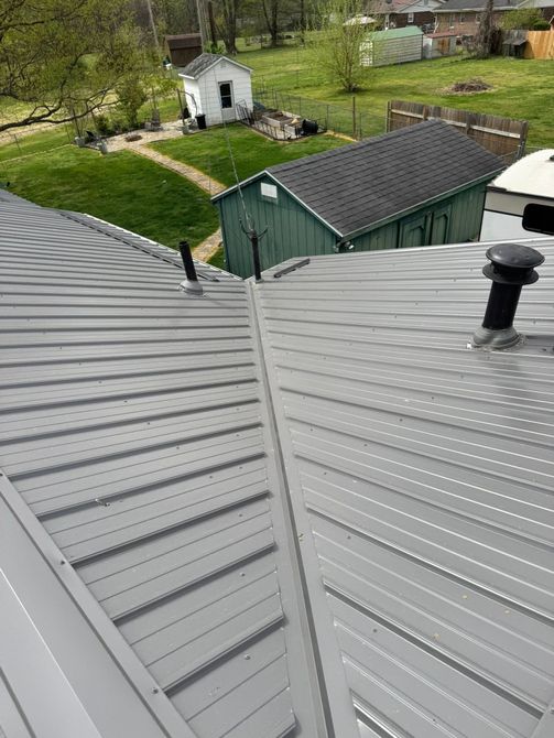 Rooftop view of gray metal roofs, a green shed, and a small white outbuilding in a grassy yard