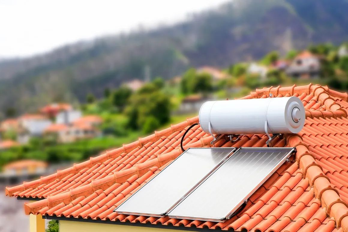 Solar water heater on a red-tiled roof with a blurred hillside neighborhood in the background