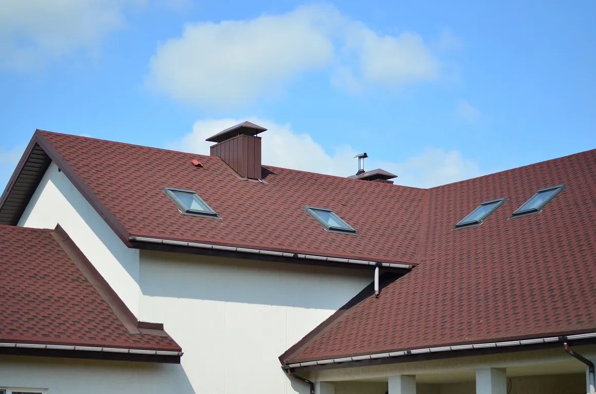 Red-tiled house roof with skylights and a chimney under a blue sky