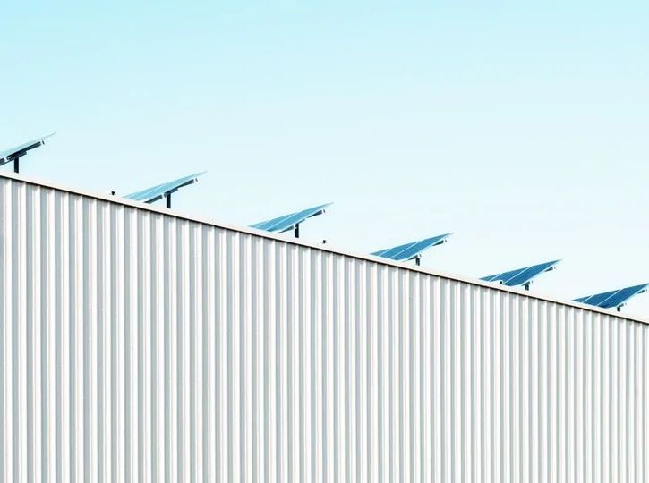 Blue solar panels atop a white corrugated roof against a pale sky