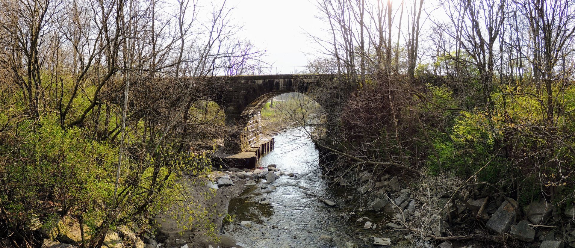 Stone arch bridge over a narrow stream in a leafless, wooded landscape