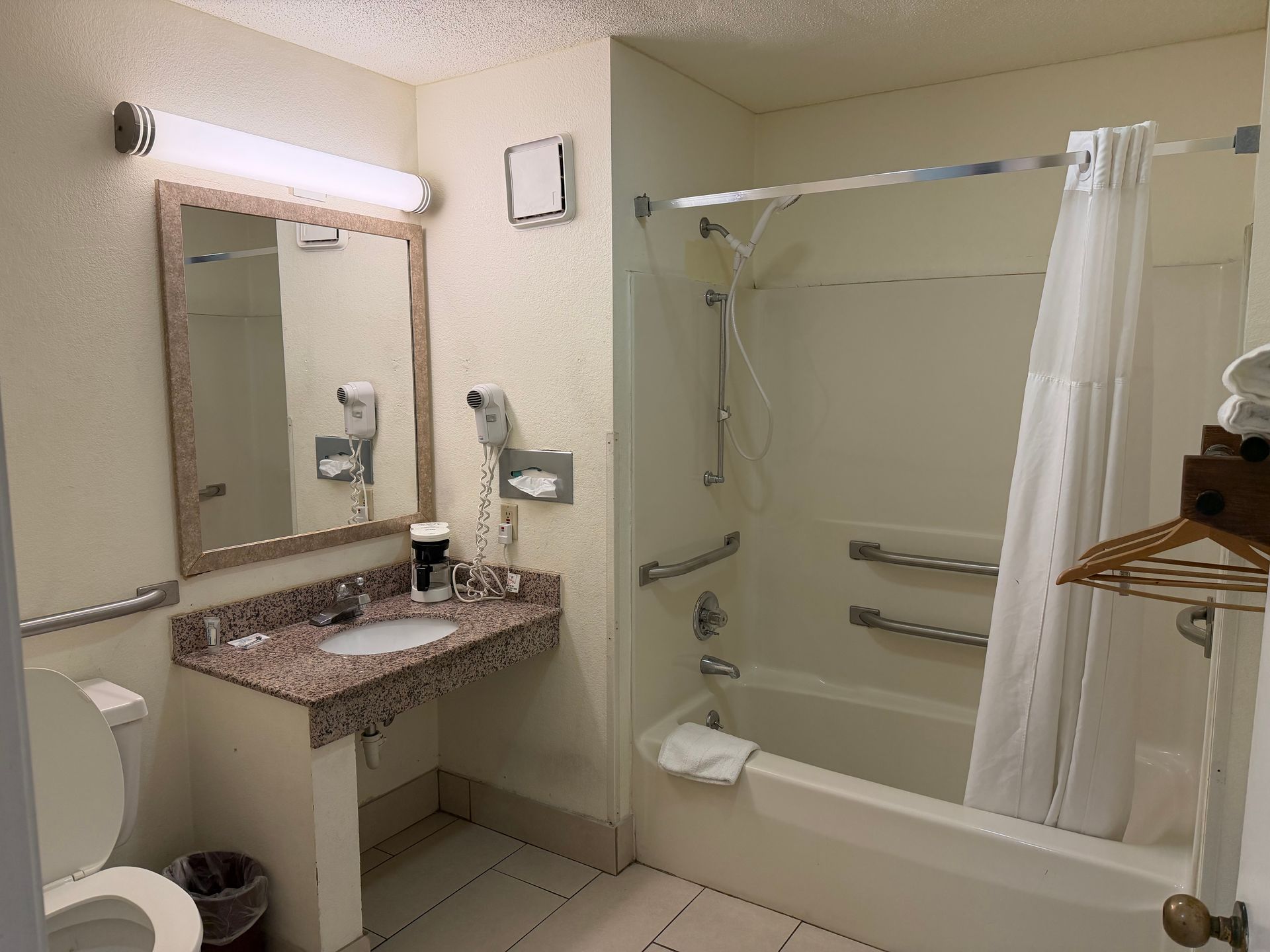 Bathroom with accessible features: tub with grab bars, low sink, mirror, toilet, and shower curtain.